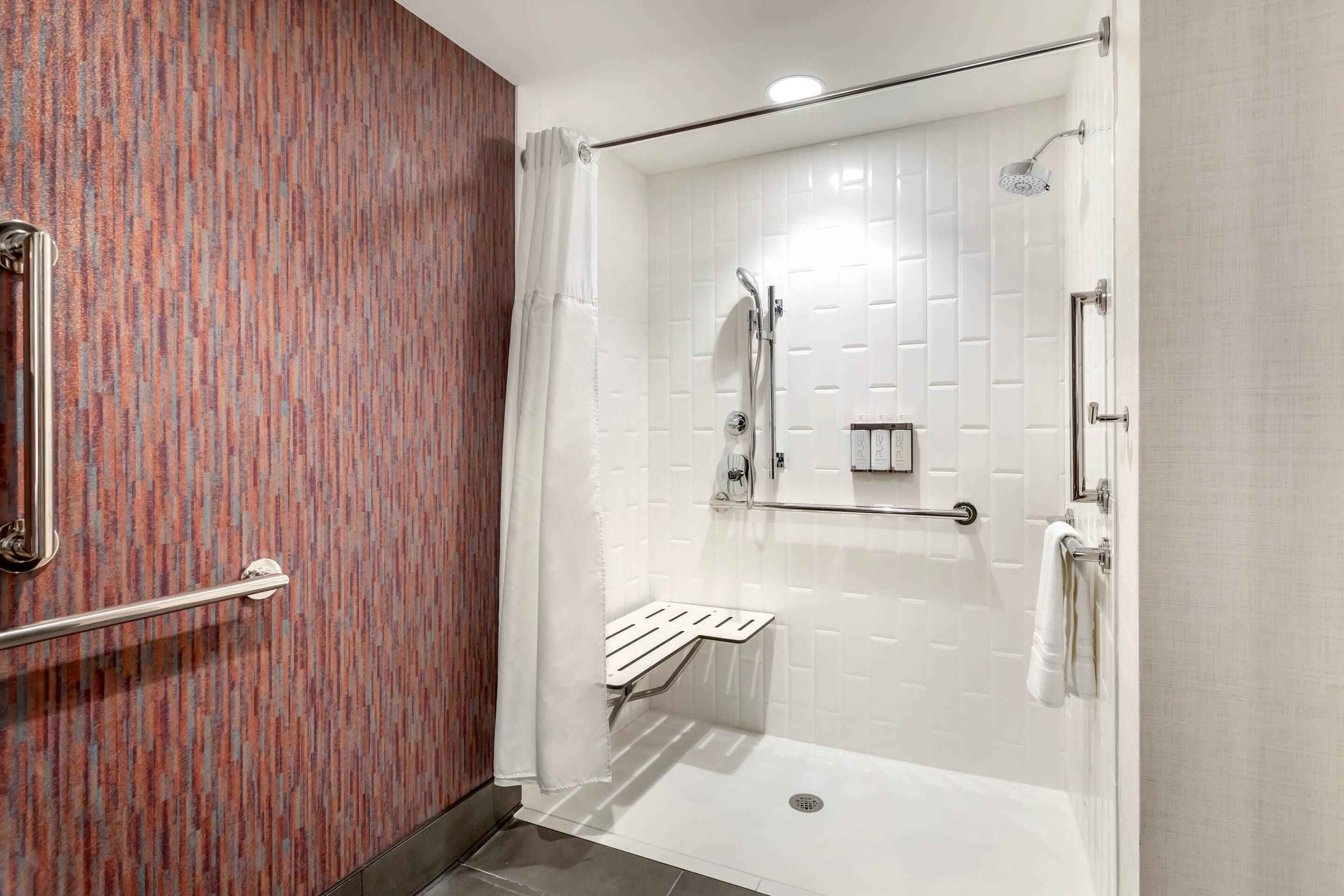 A modern bathroom with a walk-in shower, grab bars, and a towel rack.