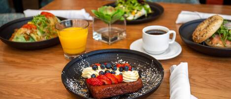 Ein Esstisch mit einer Dessertplatte, einem Orangensaftglas, einer Kaffeetasse und einem Salat.
