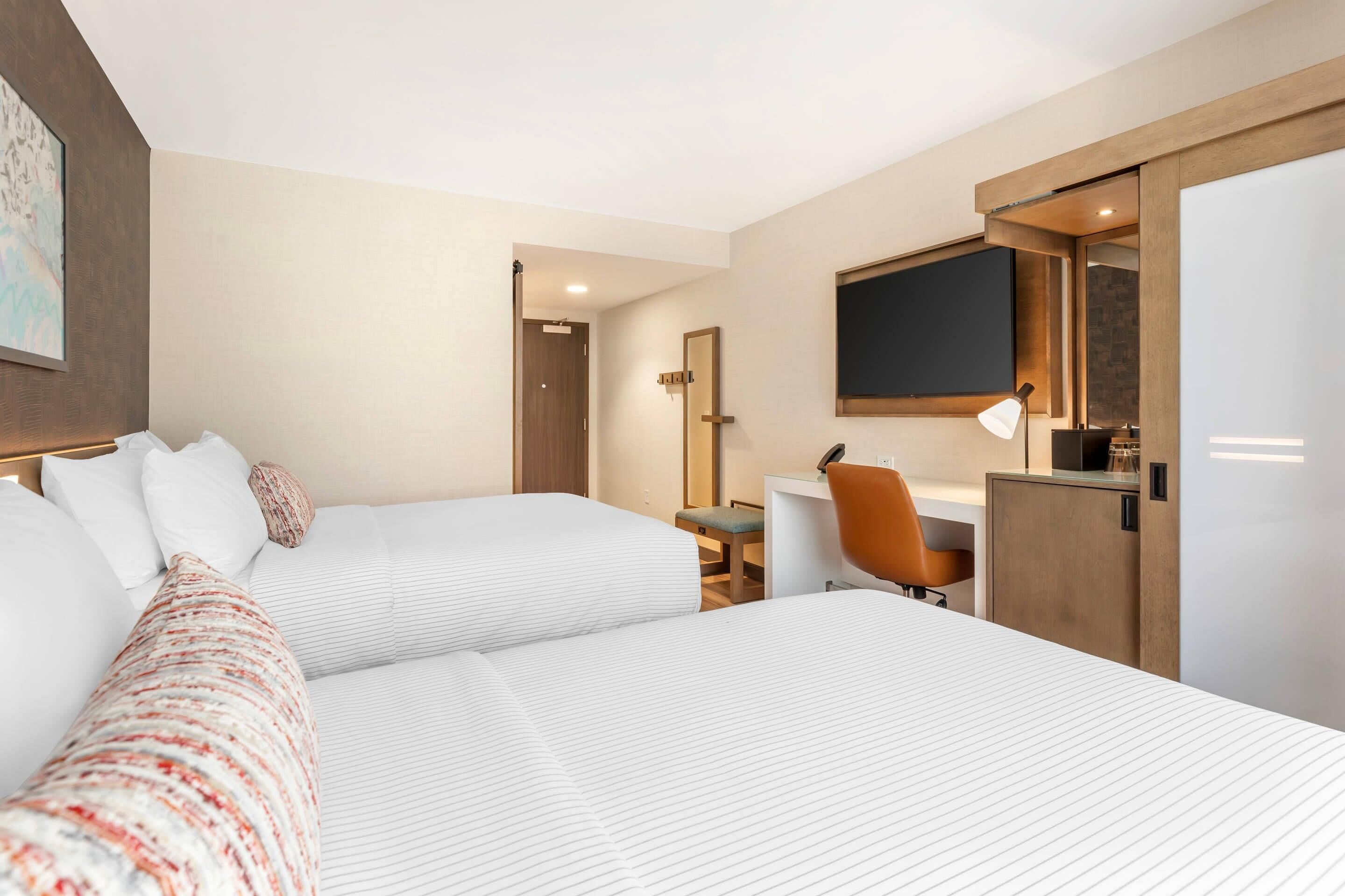 A hotel room with two beds, a desk, a chair, a TV, and a wardrobe.
