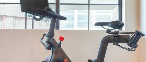 A stationary exercise bike with a digital display, positioned in a room with wooden flooring and large windows.