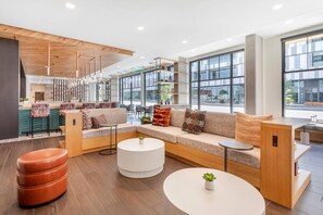 A modern lobby with a wooden ceiling, large windows, a seating area with sofas and ottomans, and a reception desk. - Cambria Hotel Denver Downtown RiNo (Denver)