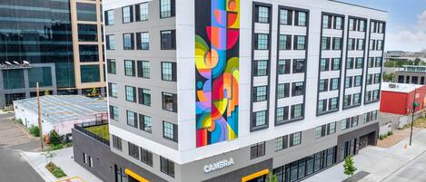 Ein modernes Gebäude mit der Aufschrift 'CAMBRIA' auf der Fassade, das auf einer Seite ein großes, vertikales, farbenfrohes Wandgemälde zeigt.