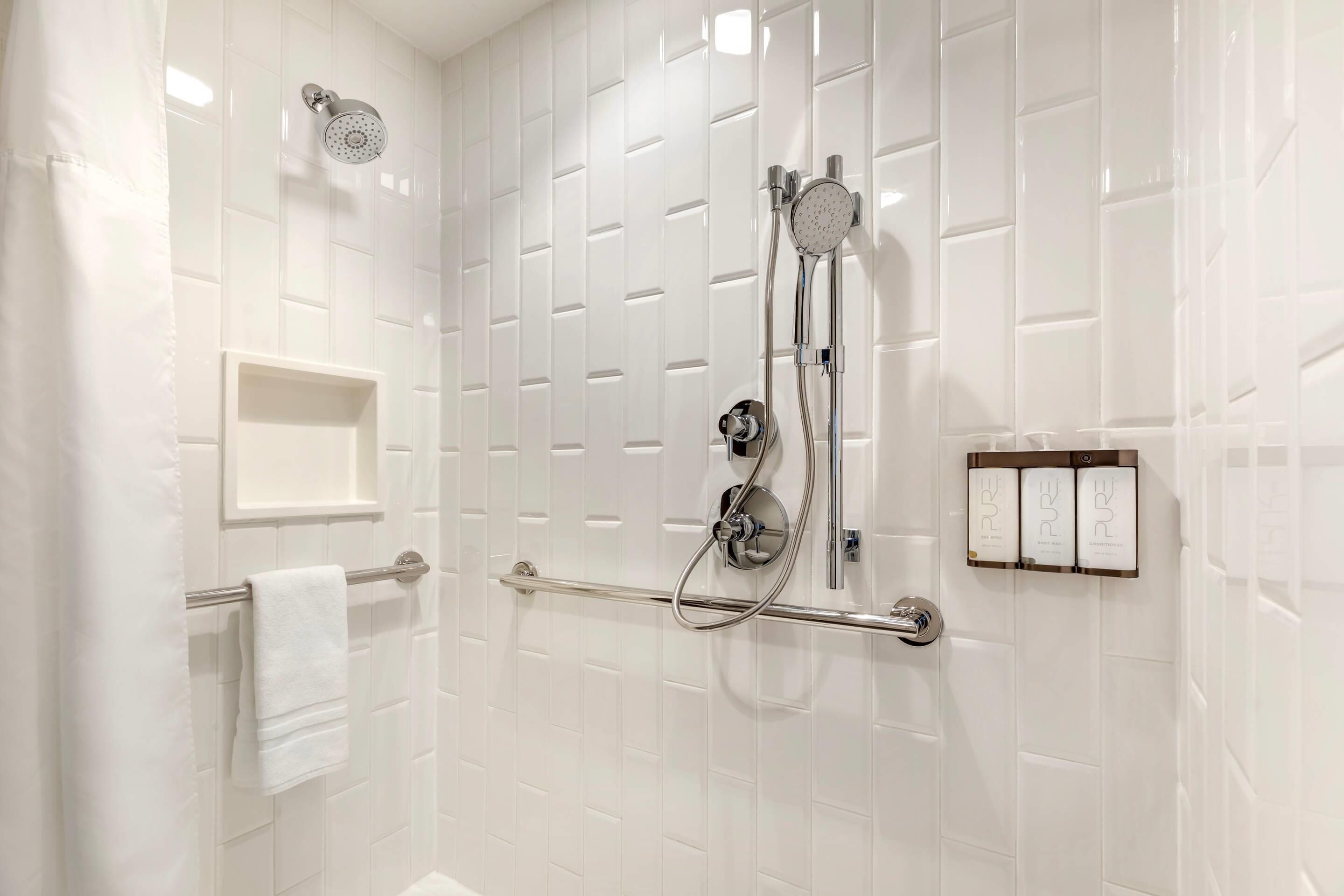 Een moderne badkamer met witte betegelde wanden, een douche met handdouche, een handdoekrek en een zeepdispenser.
