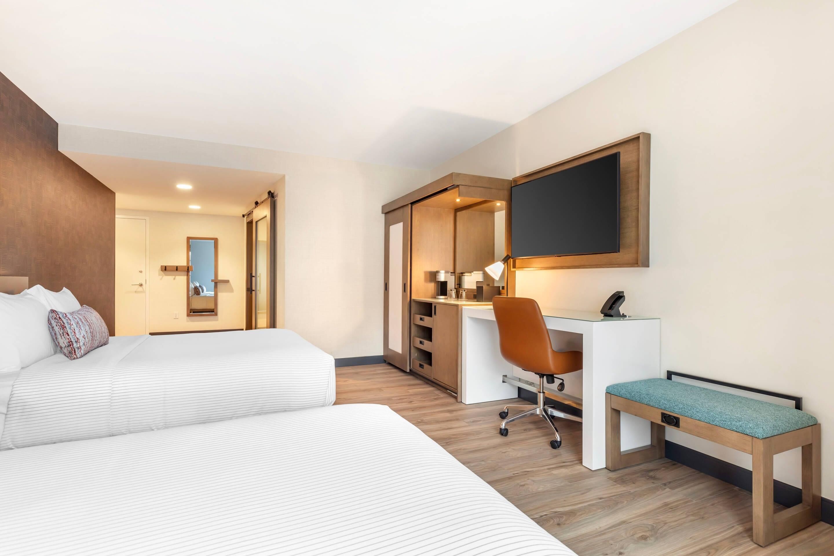 Une chambre d’hôtel équipée d’un lit, d’un bureau, d’une chaise et d’un grand miroir.