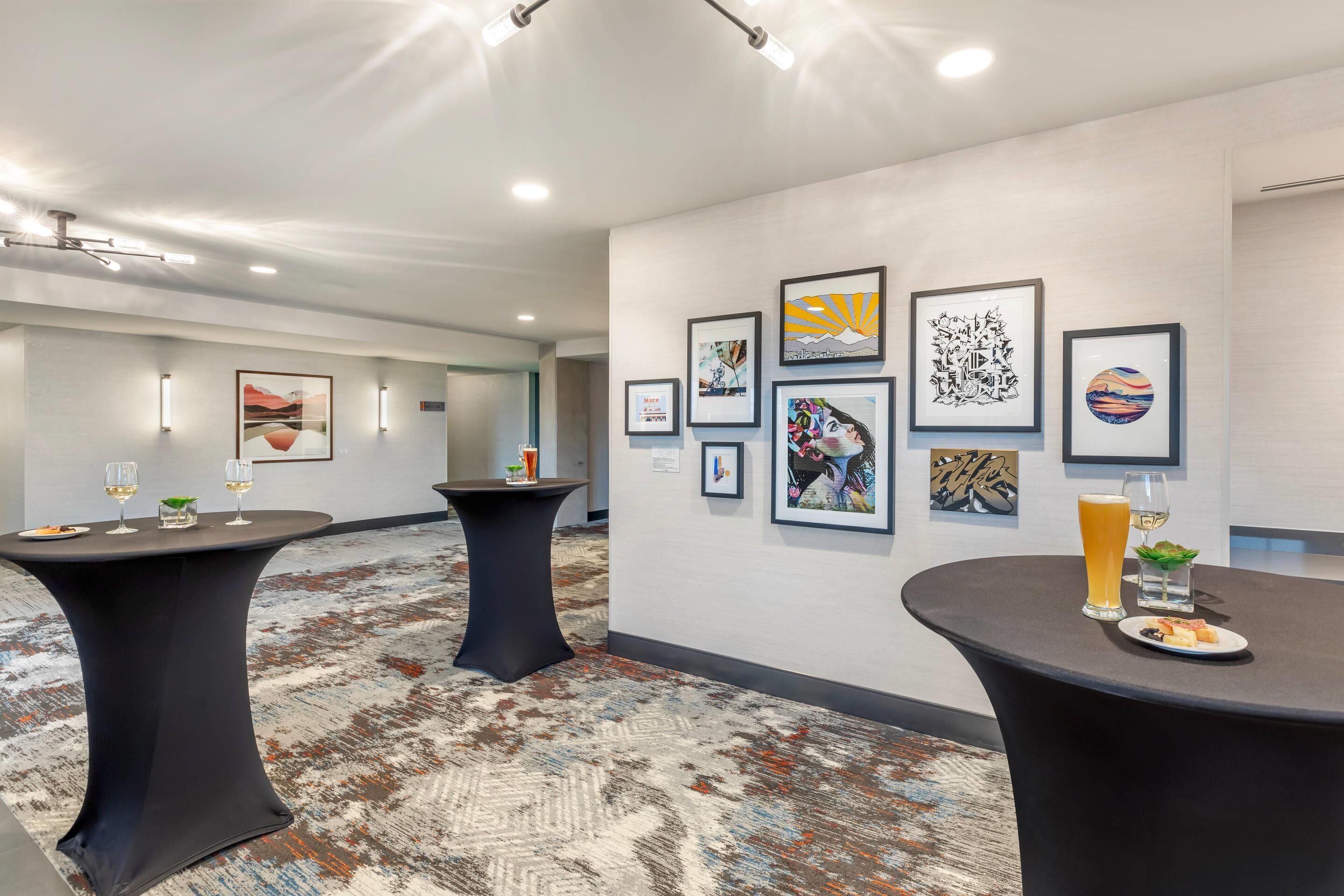 En moderne hotellobby med kunst på væggene, to runde borde med drikkevarer og et tæppe på gulvet.