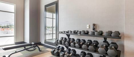 Une salle de sport équipée d’un banc, d’haltères et d’une grande fenêtre.