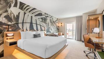 A hotel room with a large bed, a desk, a chair, a desk lamp, and a large mirror.