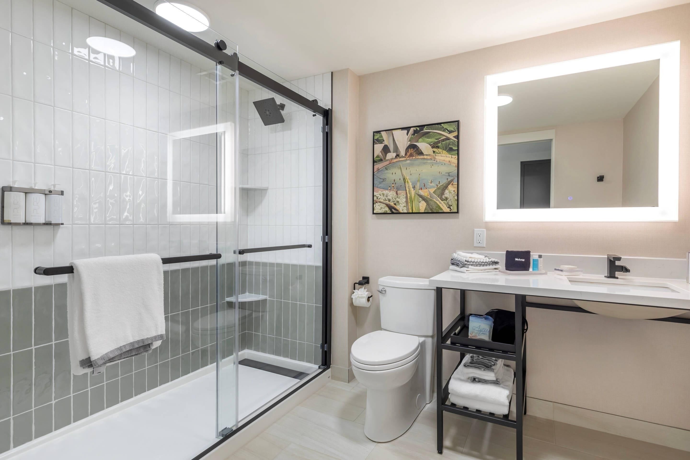 Une salle de bain moderne avec une douche à parois de verre, des toilettes, un lavabo avec un miroir et une étagère avec des serviettes.