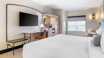 A hotel room with a large bed, a desk with a chair, a television mounted on the wall, and a window with a city view.
