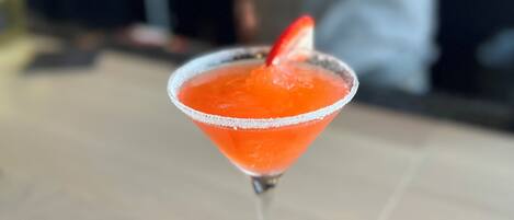 Un cóctel en una copa de martini con borde de sal y una fresa como adorno, sobre una mesa de madera.