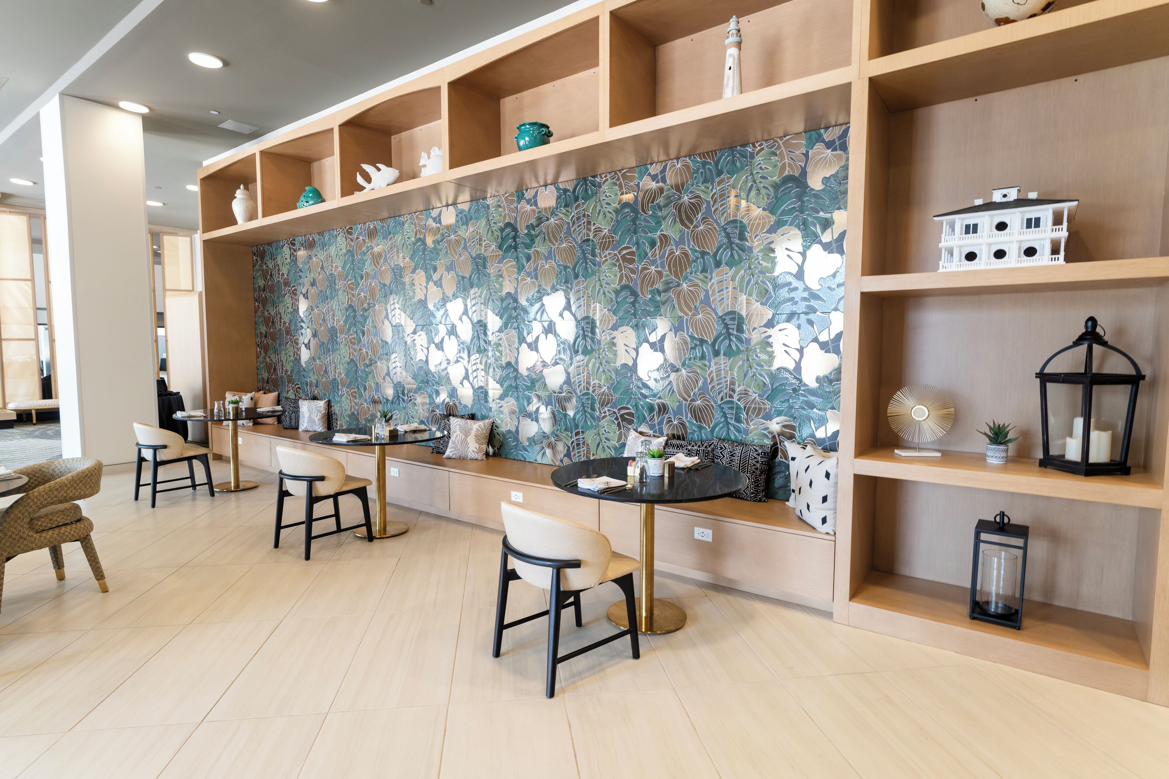 Un intérieur moderne avec un grand mur orné d’un motif floral, des étagères en bois et des coins salon.
