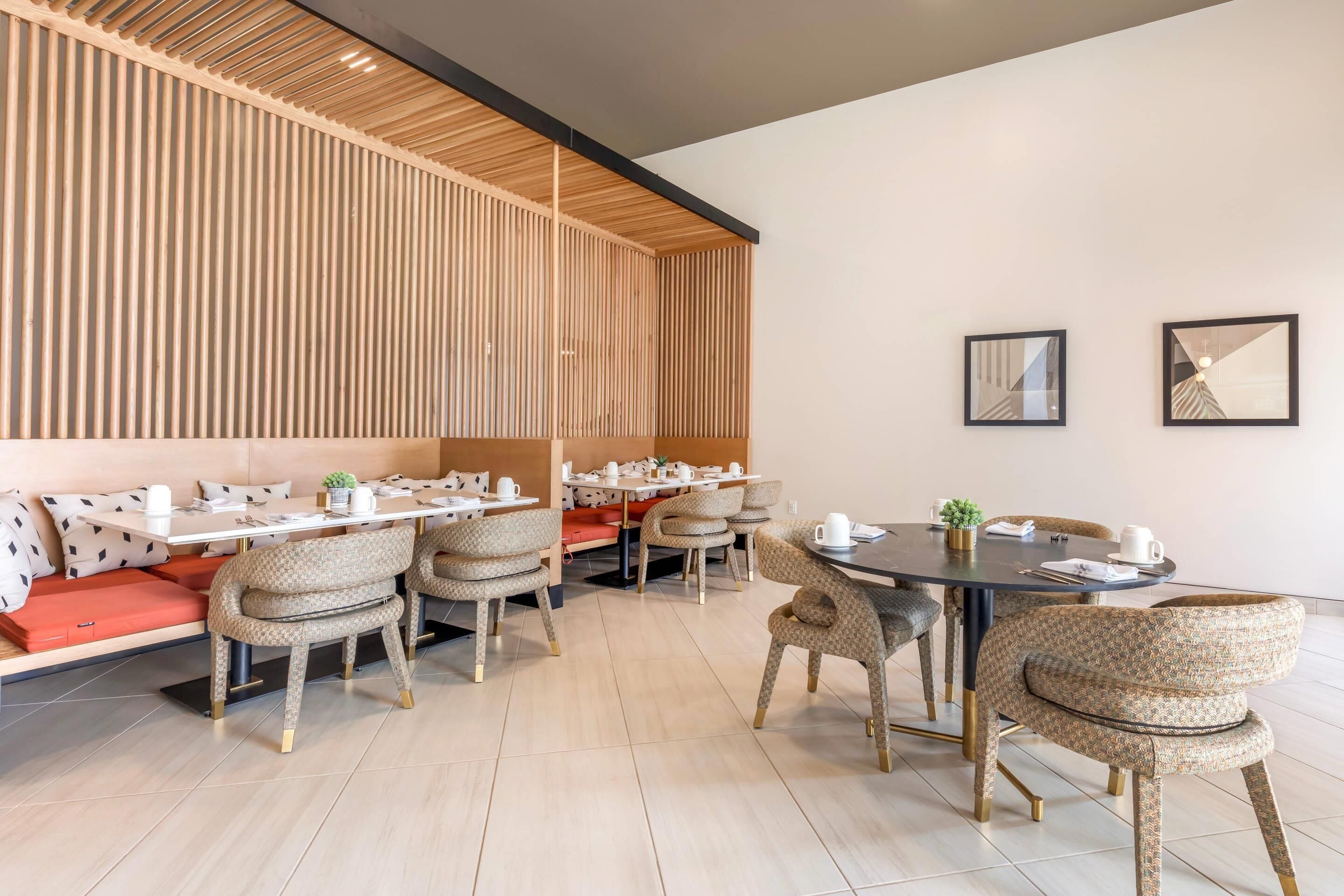 A modern dining area with wooden slats on the ceiling, cushioned seating, and a round table with chairs.