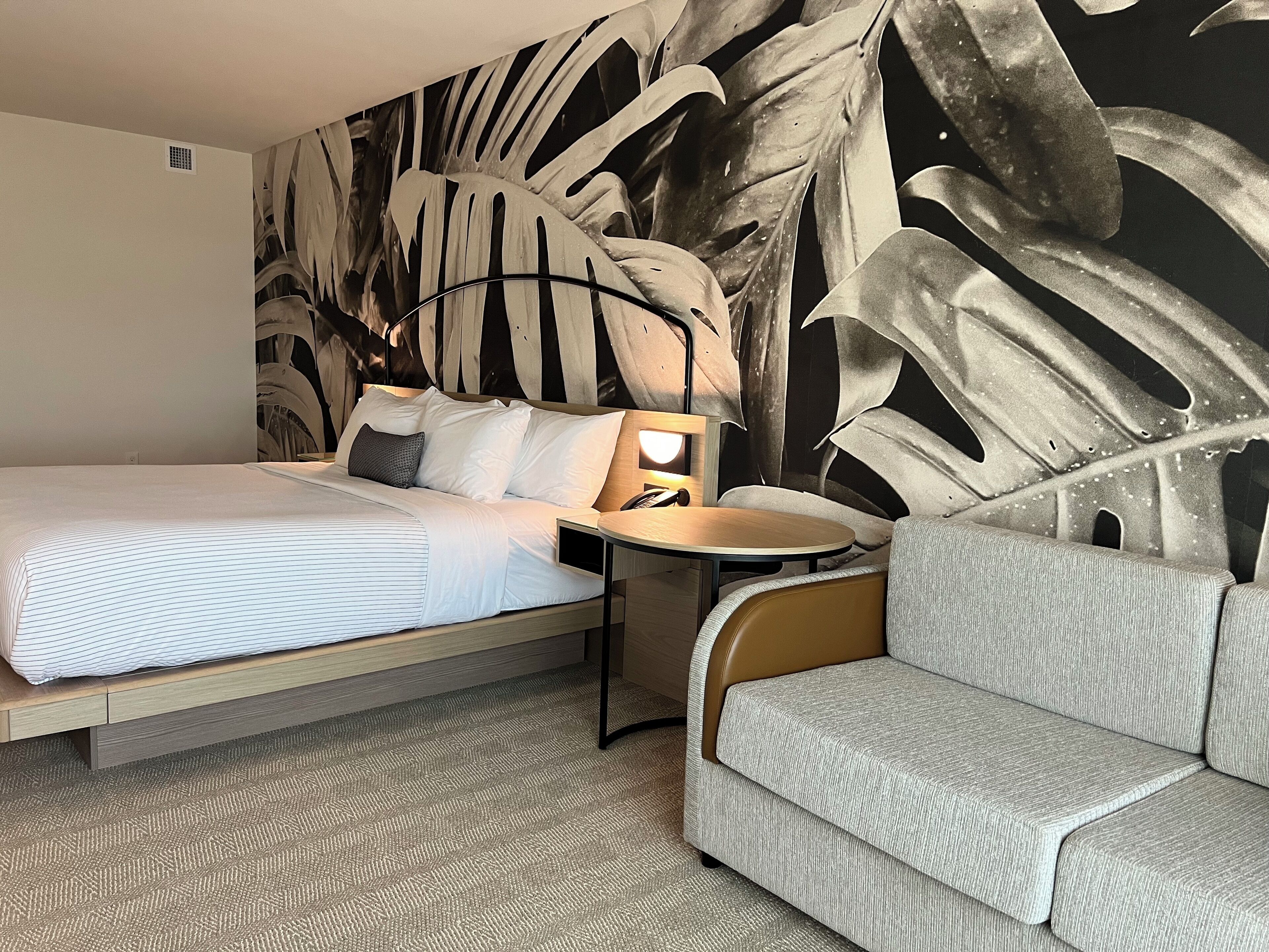 Una habitación de hotel con cama, sofá, mesita de noche y un mural en la pared.