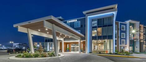 Un hotel moderno con una entrada destacada, una fachada bien iluminada y un área ajardinada en frente.