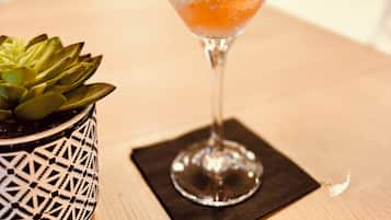 A cocktail being poured into a martini glass with a strawberry garnish on a wooden table.