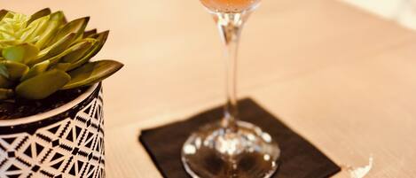 A cocktail being poured into a martini glass with a strawberry garnish on a wooden table.