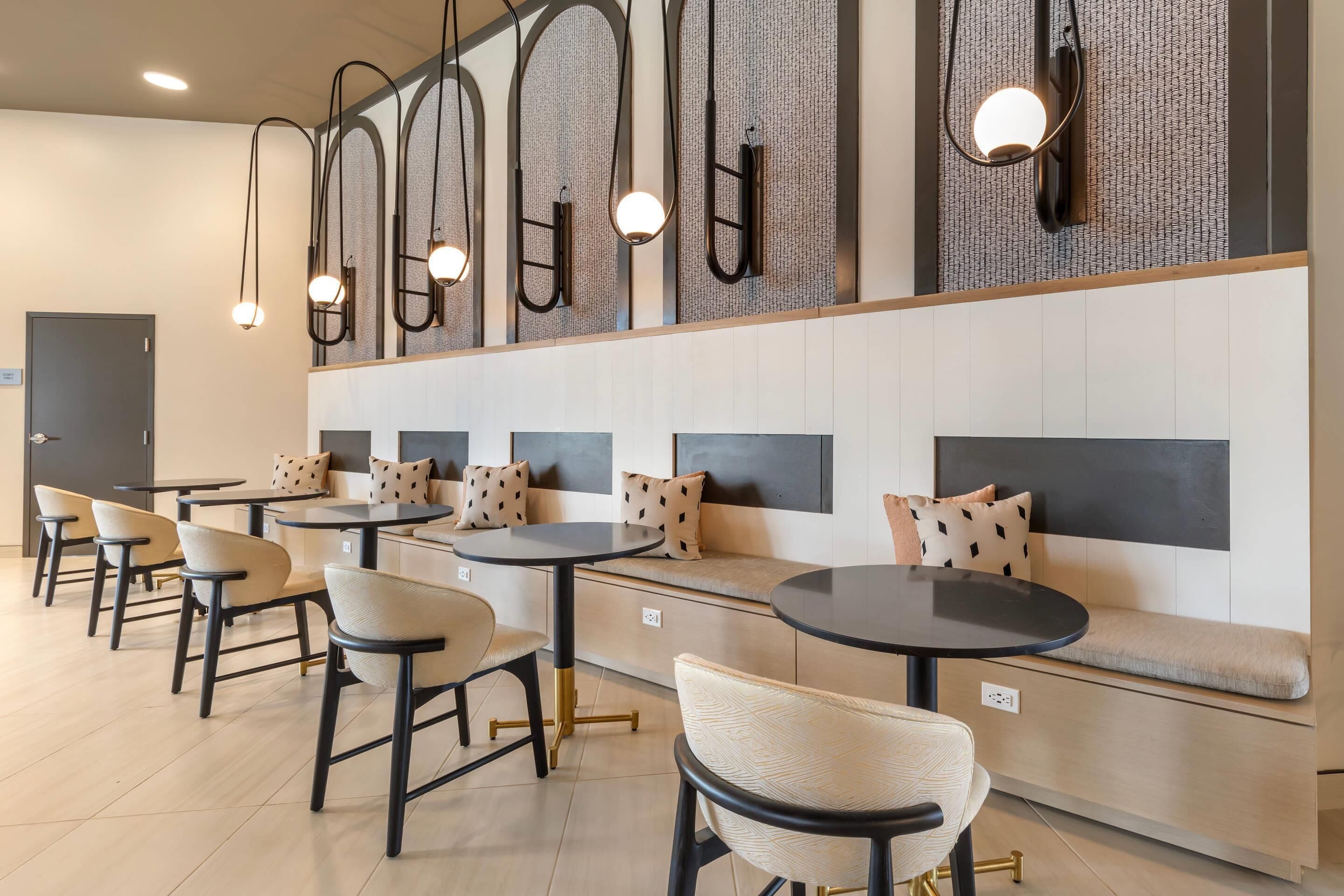 Un café moderno con mesas redondas y asientos acolchados, que cuenta con lámparas colgantes y una pared con textura.