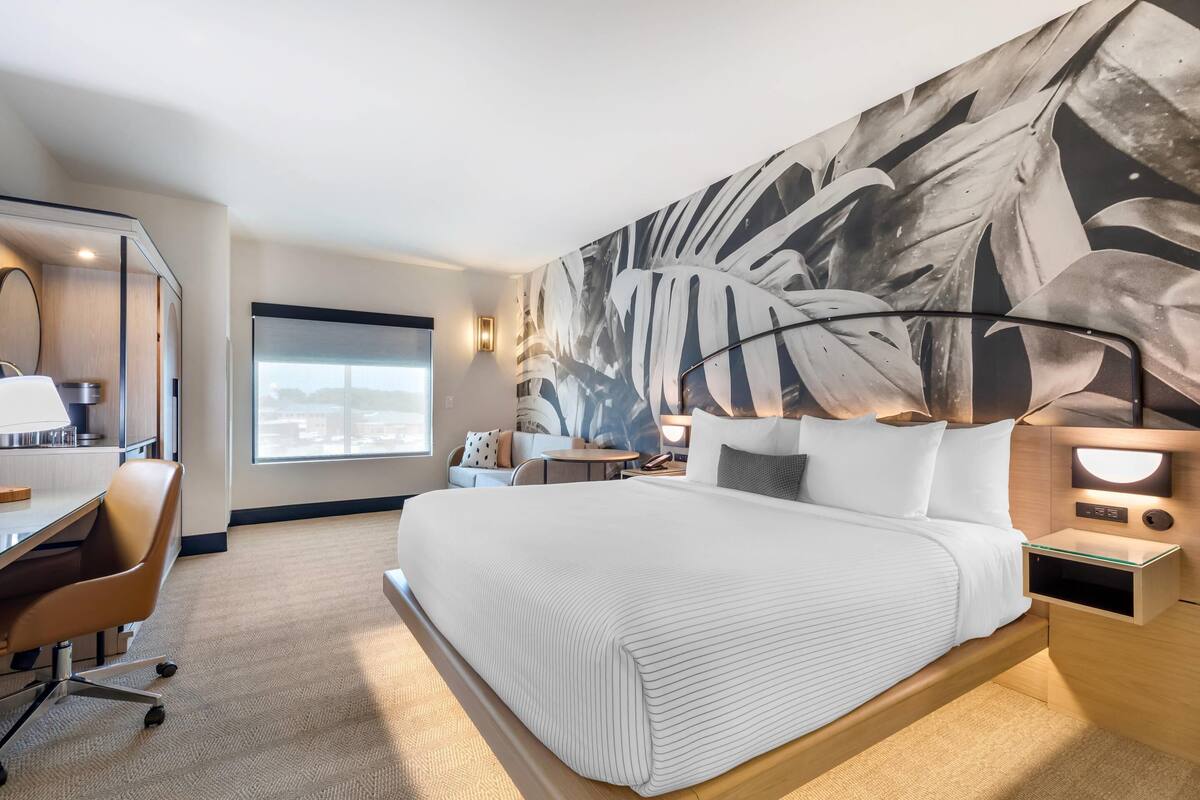 A modern hotel room with a large bed, a desk, and a view of the city.