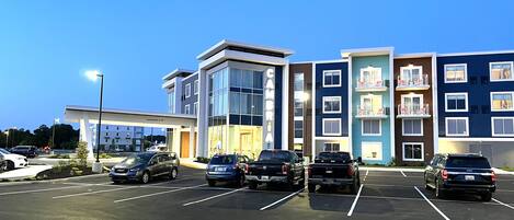 A multi-story hotel with a modern design, featuring a parking lot with several cars.