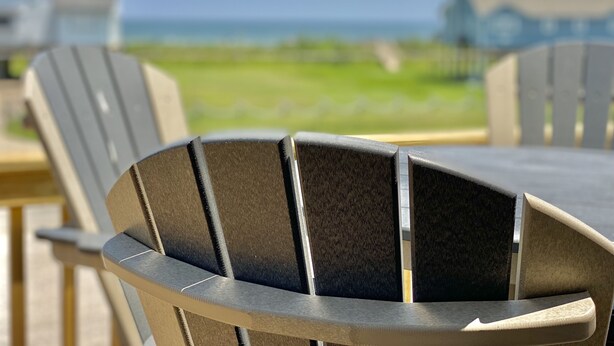 A close-up of a modern outdoor chair with a metal frame and dark cushion, part of a dining set.