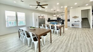 A modern kitchen with white cabinets, a stainless steel refrigerator, and a dining area with a wooden table and white chairs.