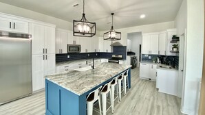 A modern kitchen with white cabinets, a blue island, stainless steel appliances, and pendant lighting.