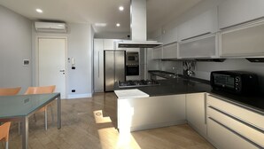 Una cocina moderna con electrodomésticos de acero inoxidable, un comedor con mesa de vidrio y vistas al salón.