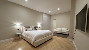 Un dormitorio moderno con una cama grande, mesitas de noche, un sofá y un televisor montado en la pared.