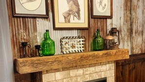 A fireplace with framed wildlife prints, green glass bottles, and a rustic wooden mantel. - Briar Patch Cabin RRG: Firepit, Sunset, WIFI (Stanton)