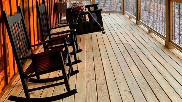 A wooden deck with rocking chairs and a table, overlooking a forested area. - Briar Patch Cabin RRG: Firepit, Sunset, WIFI (Stanton)