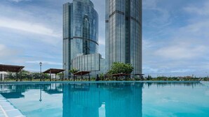 A modern hotel with a large swimming pool, two tall skyscrapers in the background, and outdoor seating areas. - Hilton Brazzaville Les Tours Jumelles Hotel & Residences (Brazzaville)