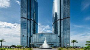 A modern hotel with two tall glass buildings, a central fountain, and a clear blue sky. - Hilton Brazzaville Les Tours Jumelles Hotel & Residences (Brazzaville)