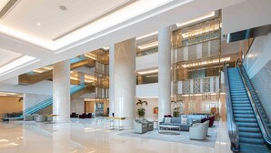 A spacious lobby with a central seating area, multiple floors, and an escalator. - Hilton Brazzaville Les Tours Jumelles Hotel & Residences (Brazzaville)