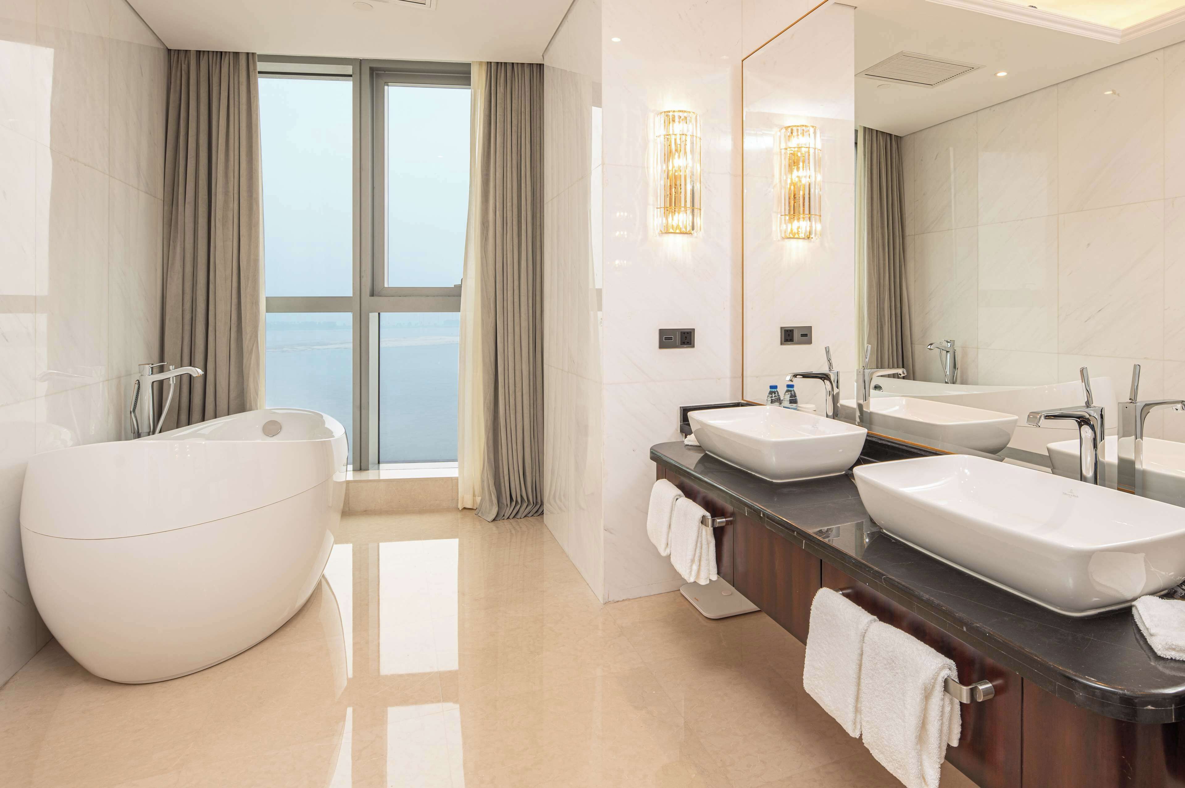 A modern bathroom with a freestanding bathtub, two sinks, and a large mirror.