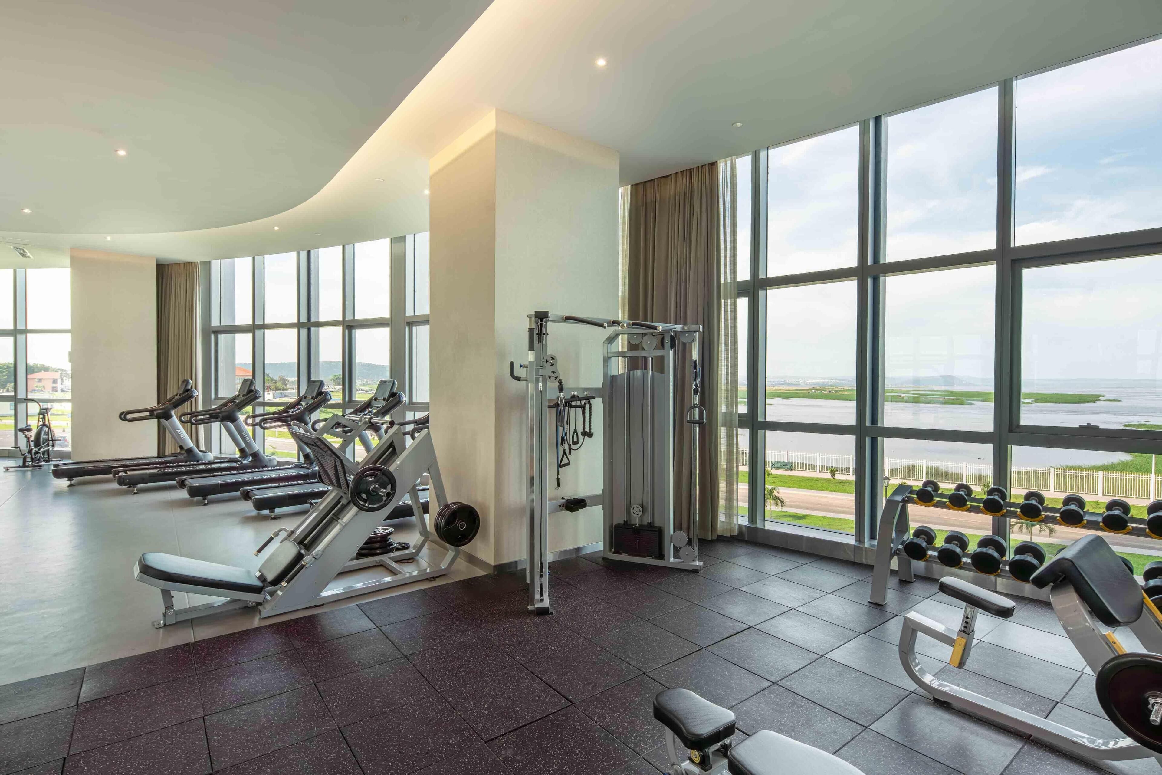A gym with various exercise equipment, large windows, and a view of a body of water.