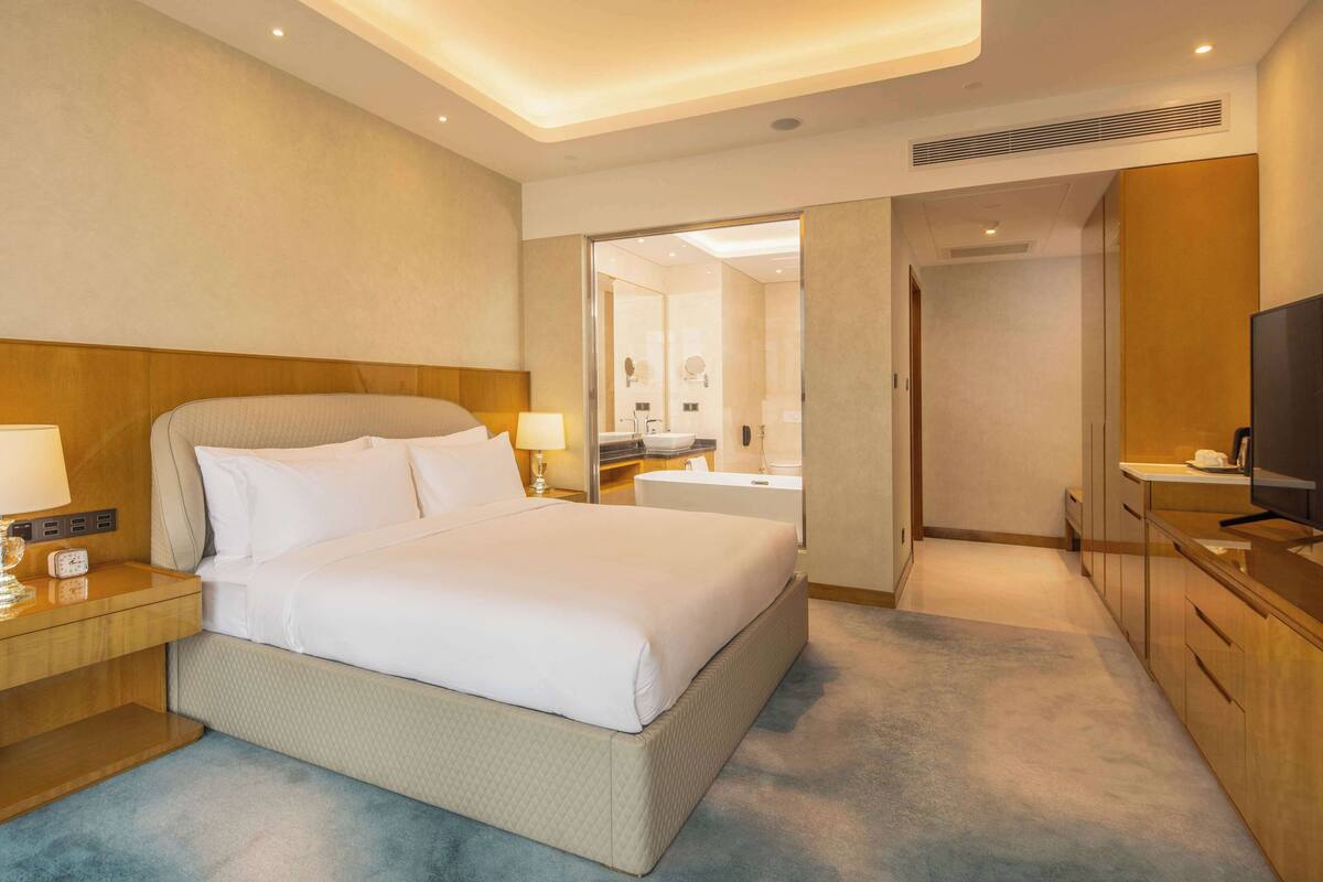 A hotel room with a bed, bedside table, lamp, and a television.