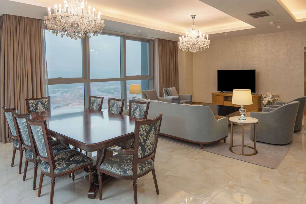 A spacious living room with a large dining table, comfortable seating, a flat-screen TV, and a view of the ocean.