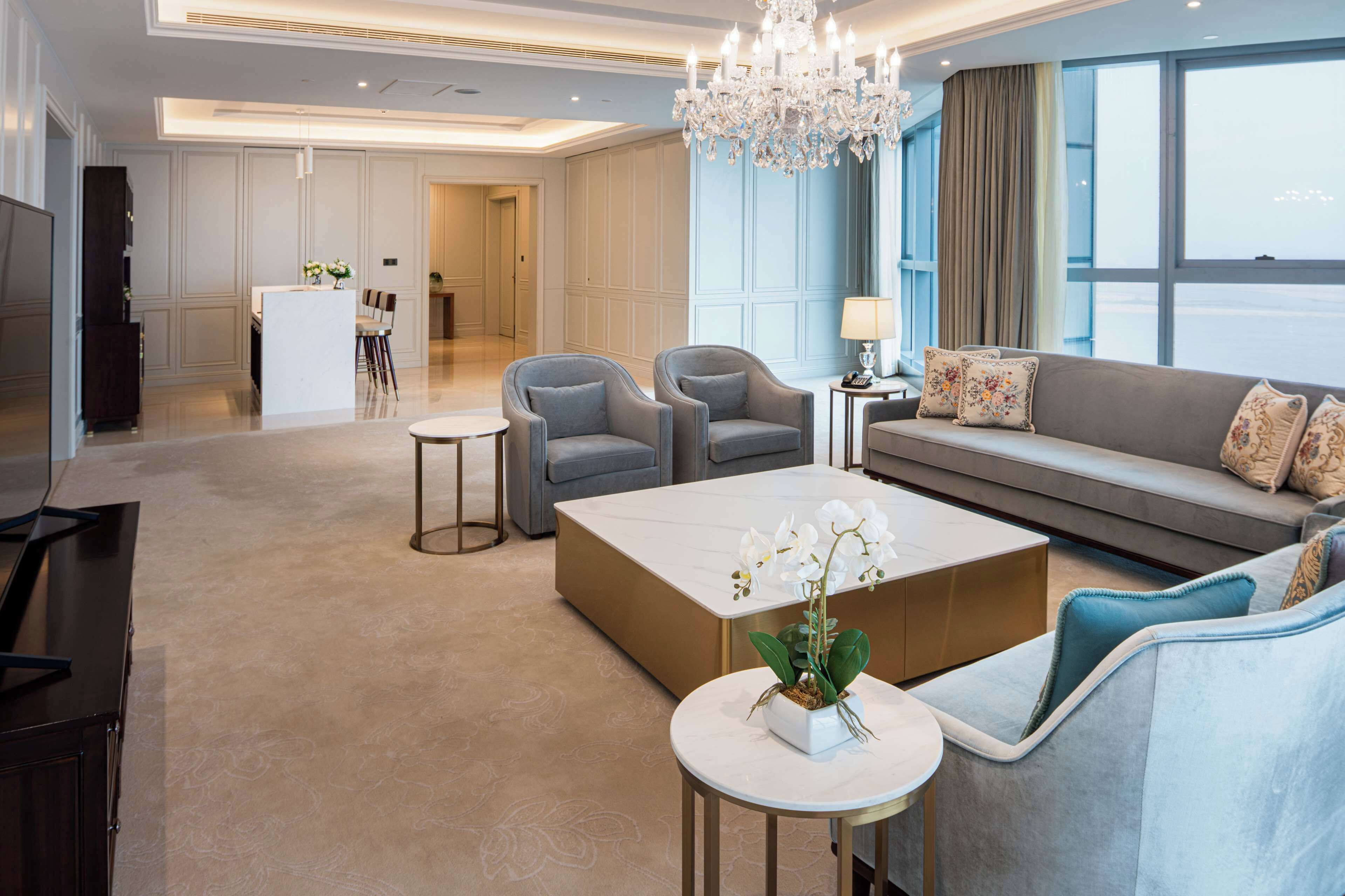 A spacious living room with a sofa, armchairs, a coffee table, and a chandelier.