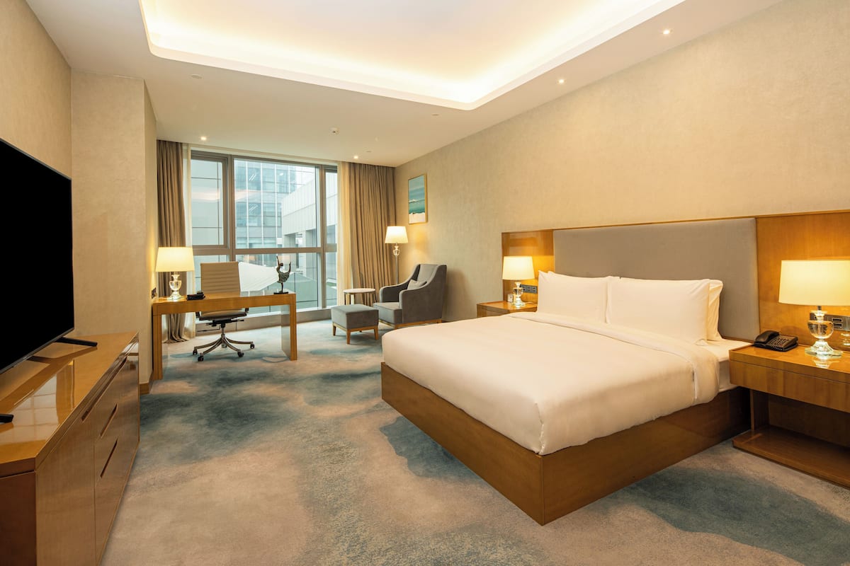 A hotel room with a large bed, a desk with a chair, a TV, and a window with curtains.