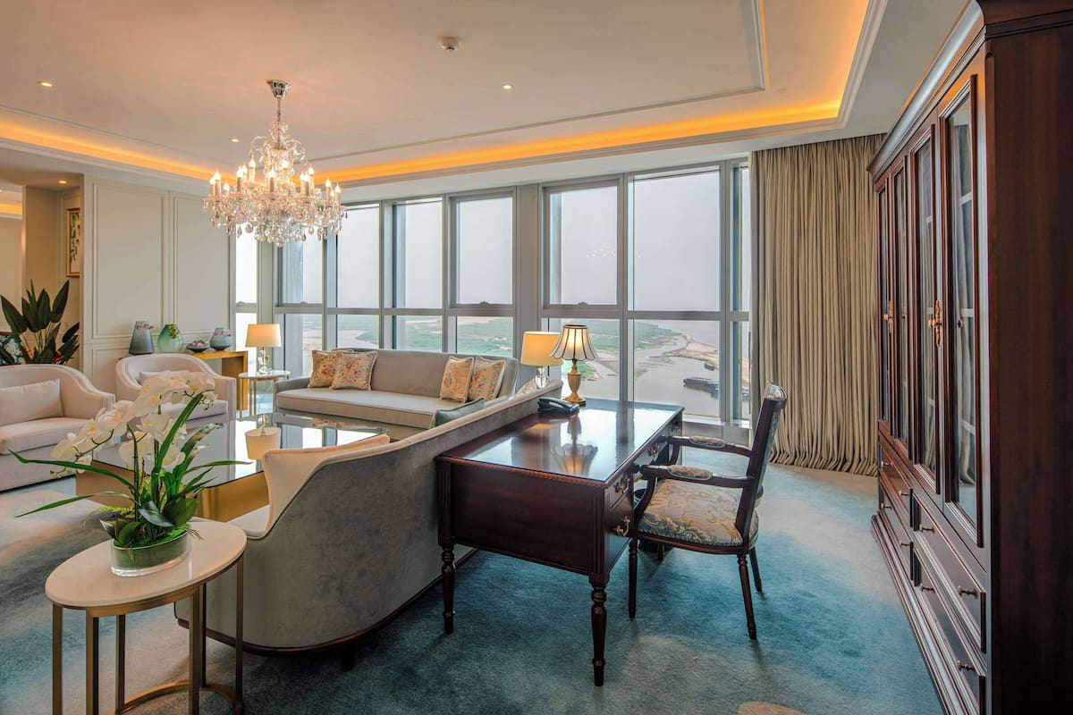 A spacious living room with a large window, a chandelier, and a view of the ocean.