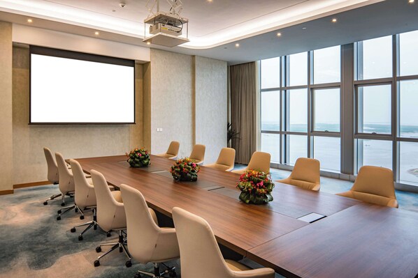 Une salle de conférence dotée d’une longue table, de nombreuses chaises, d’un écran de projection et de grandes fenêtres offrant une vue sur la mer.