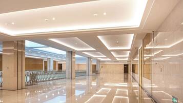 A spacious, modern lobby with a high ceiling, reflective flooring, and a glass railing overlooking a lower level.