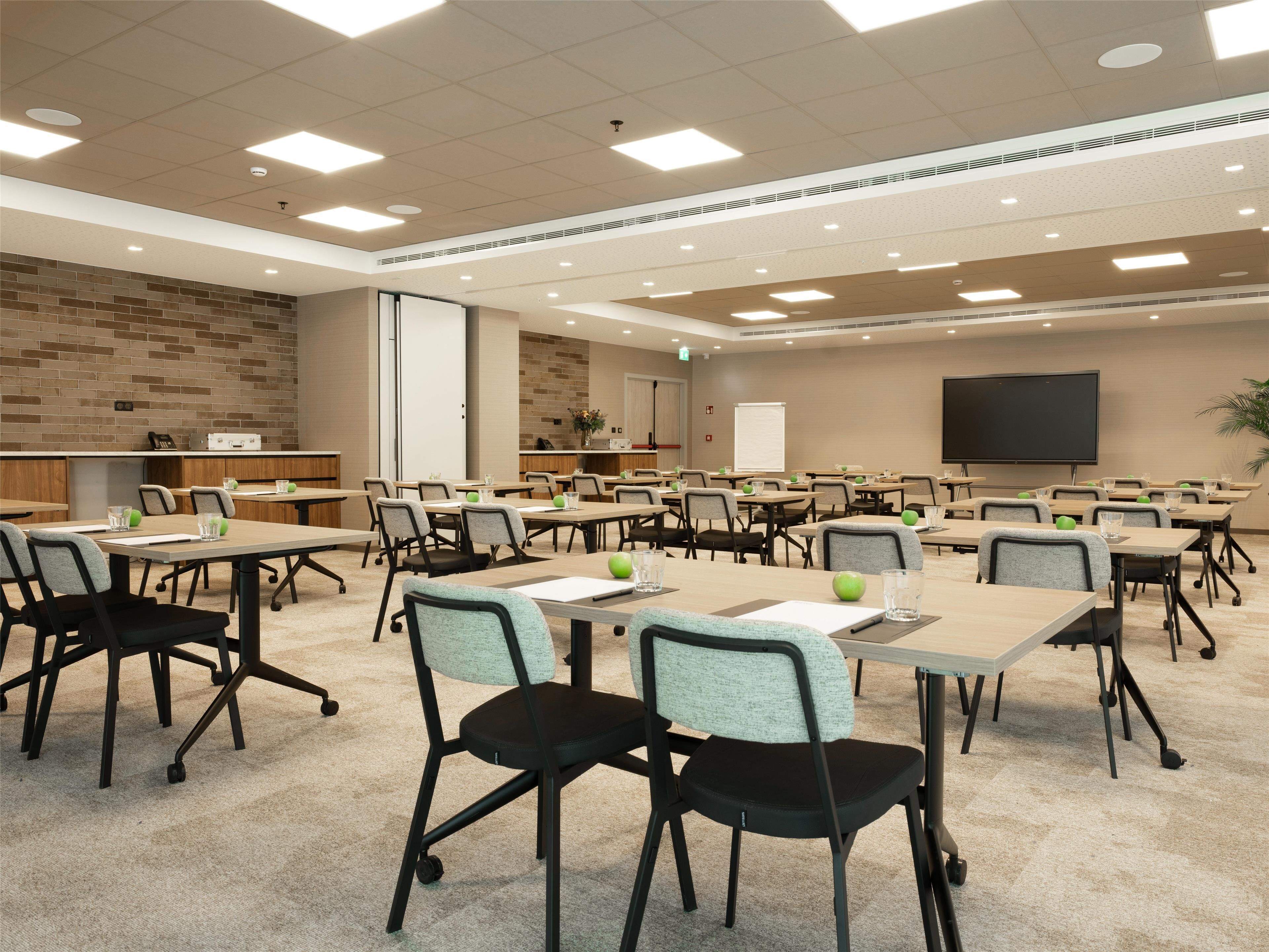 Un salón de conferencias con varias mesas y sillas, equipado con proyectores y una pantalla grande.