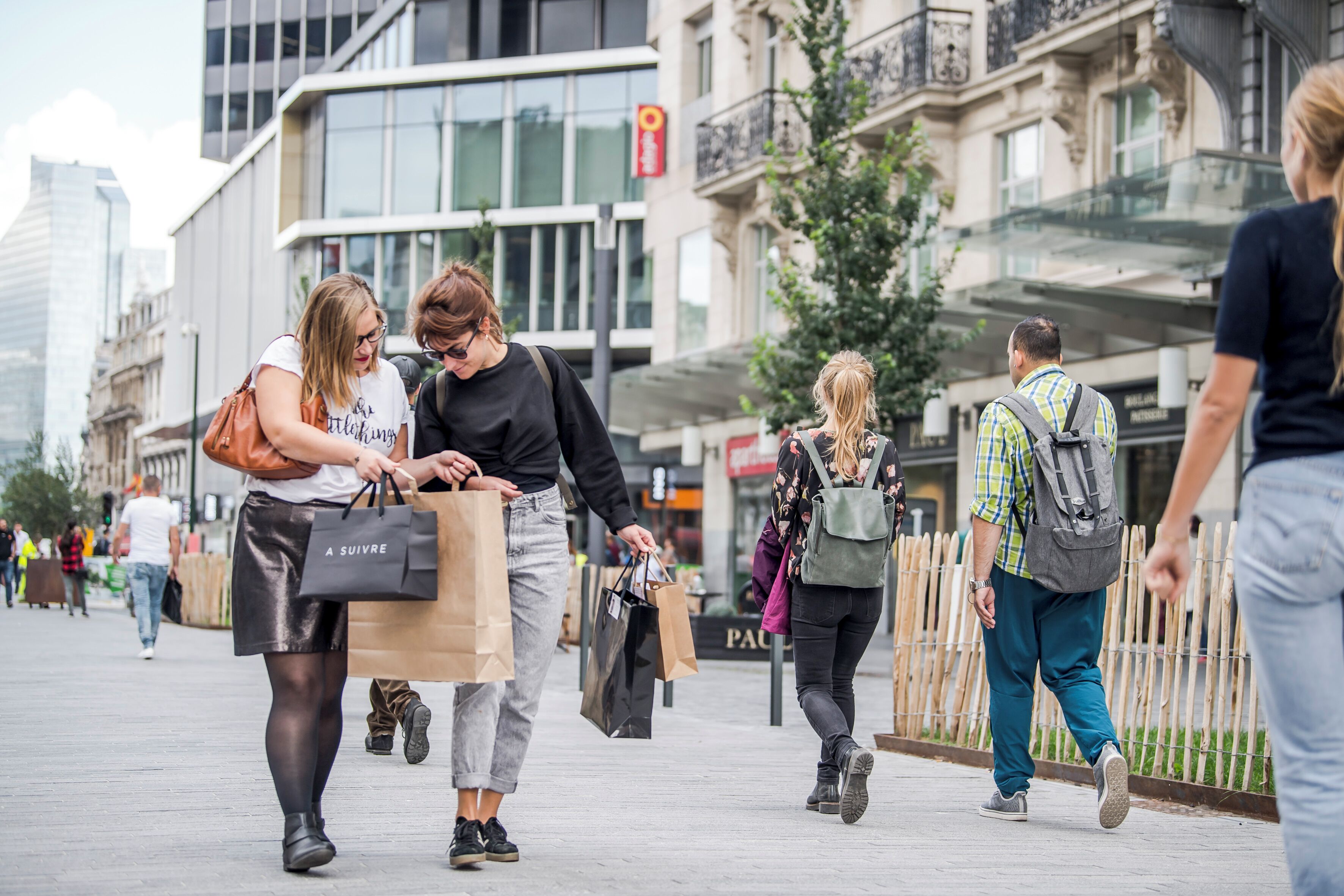 A busy urban street with pedestrians, some carrying shopping bags.