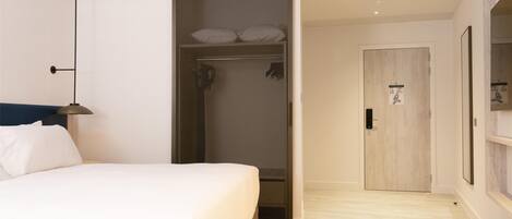 A modern hotel room with a bed, a walk-in closet, and a shower area.