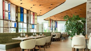A modern restaurant with a long counter, cushioned seating, and a large green plant. - Hilton Garden Inn Brussels Airport (Machelen)