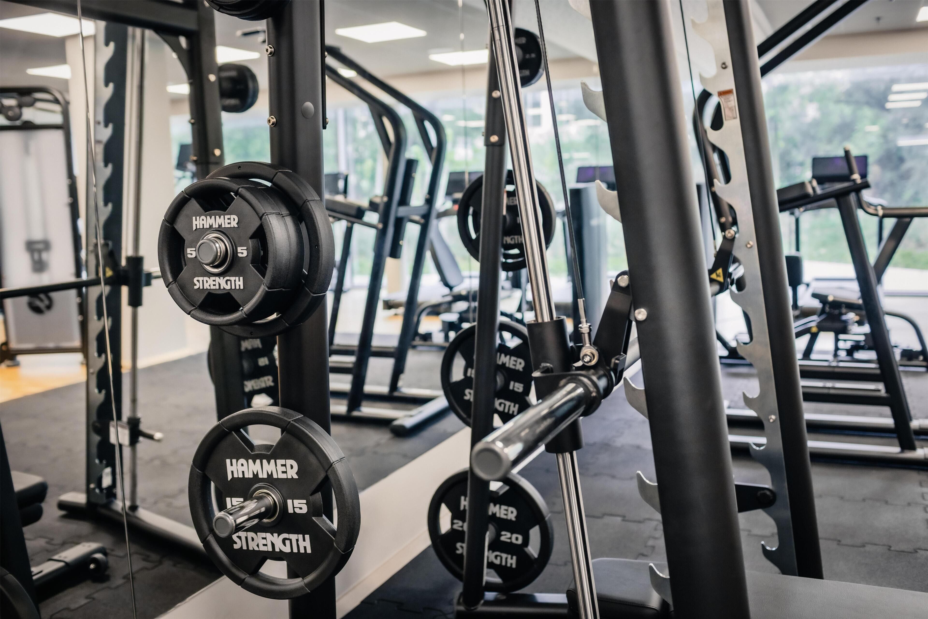 Un gimnasio con equipo de levantamiento de pesas, incluyendo una prensa de banca y mancuernas con la etiqueta 'HAMMER STRENGTH'.