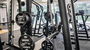 Un gimnasio con equipo de levantamiento de pesas, incluyendo una prensa de banca y mancuernas con la etiqueta 'HAMMER STRENGTH'.