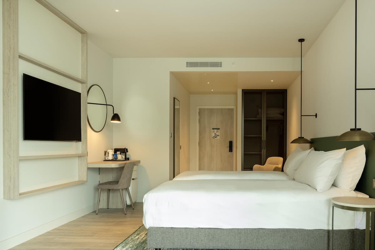 Ein modernes Hotelzimmer mit einem großen Bett, einem Schreibtisch mit Stuhl, einem an der Wand montierten Fernseher und einem Kleiderschrank.