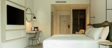 A modern hotel room with a large bed, a desk with a chair, a television mounted on the wall, and a wardrobe.